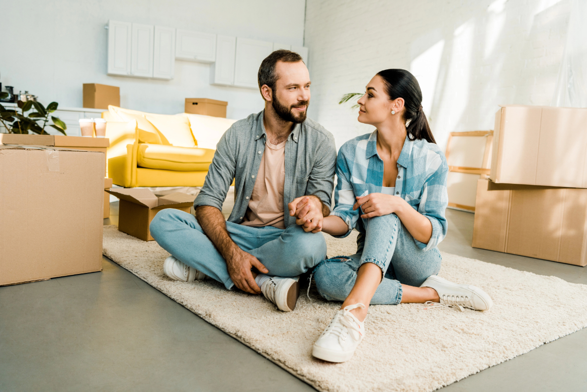 Husband and wife sitting on floor and holding hands while packing for new house